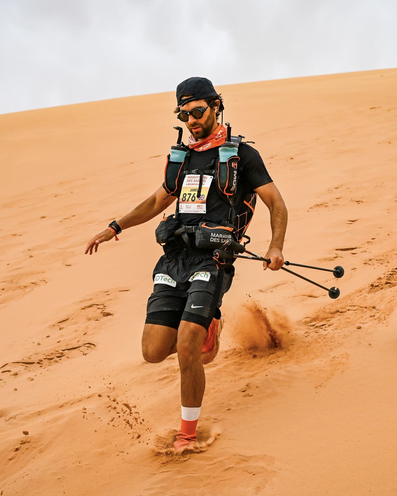 James Jackson running down a sand dune with poles on the Marathon des Sables